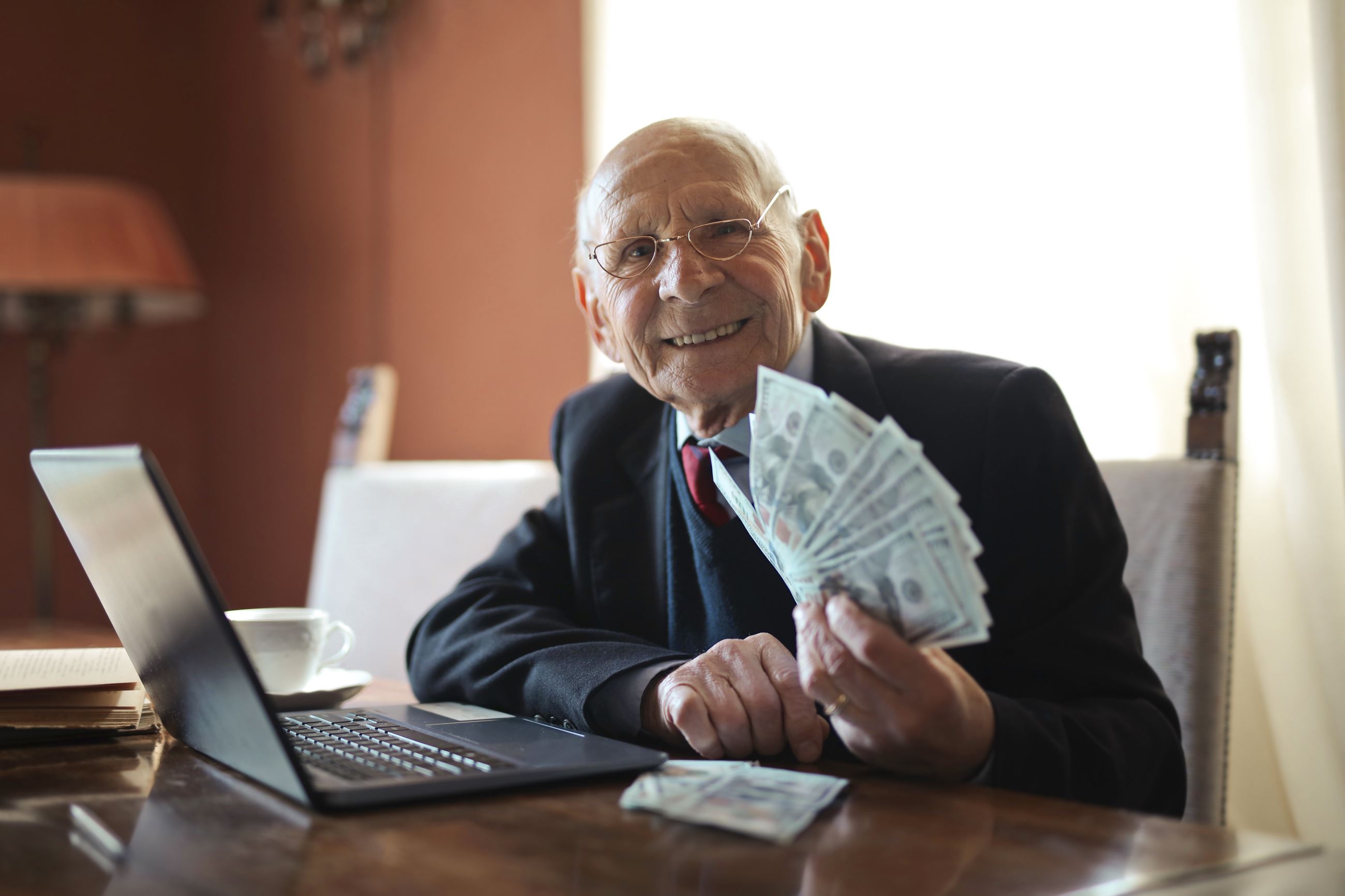 Pexels.com - Elderly gentleman at a desk with a handful of dollar bills