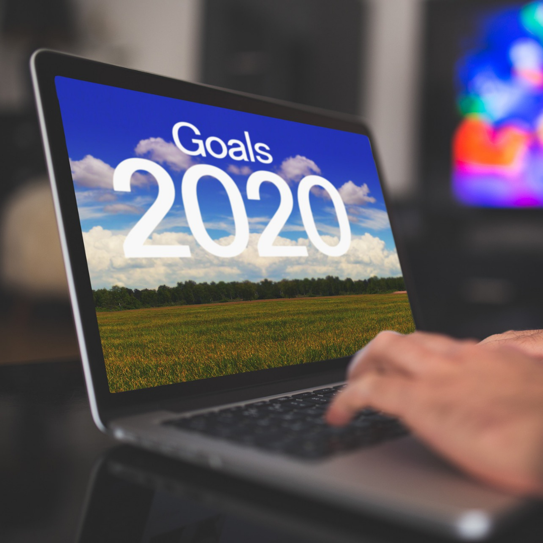 Laptop on a table with Goals 2022 on screen, two hands typing, fuzzy multicolor lights in background